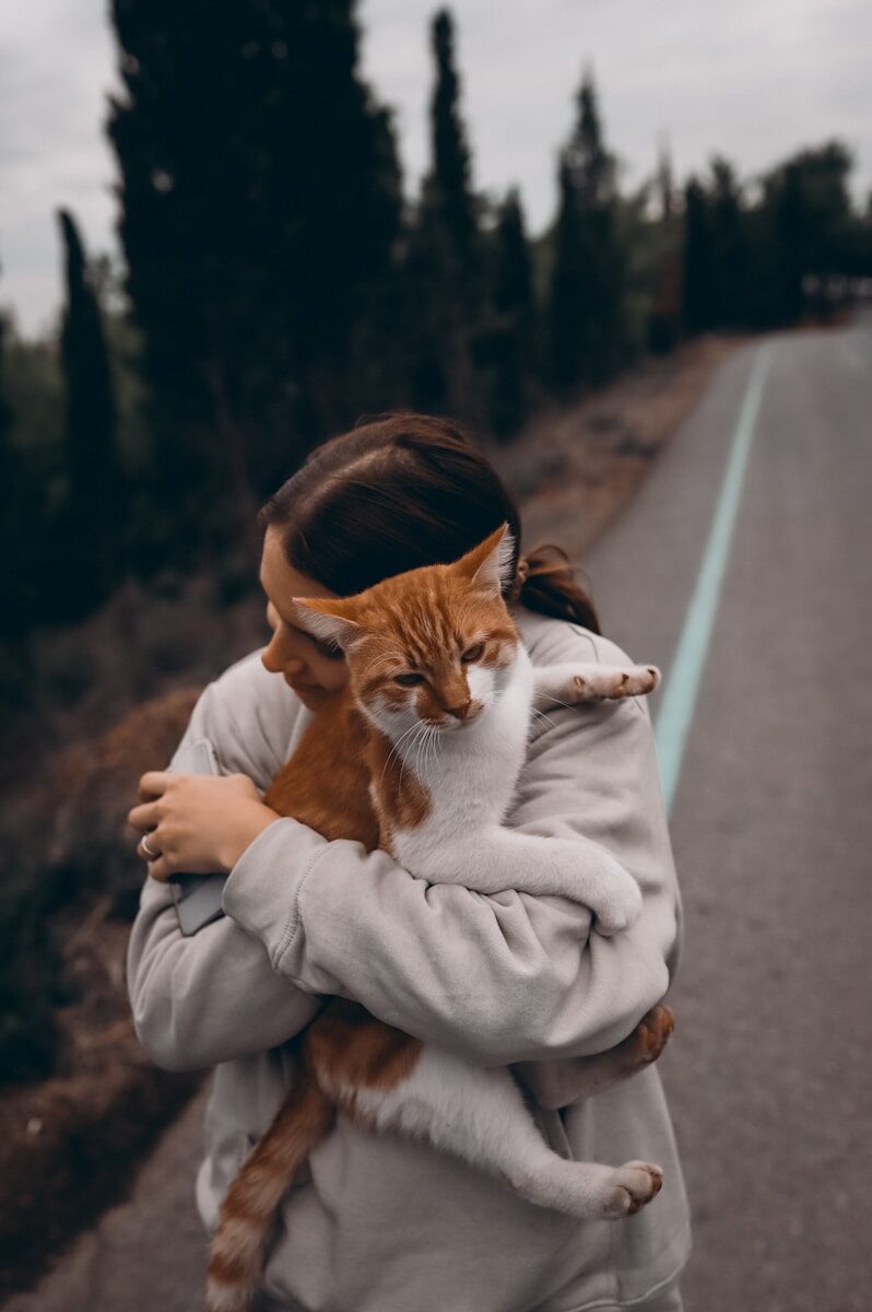 a woman holding a cat on the side of a road